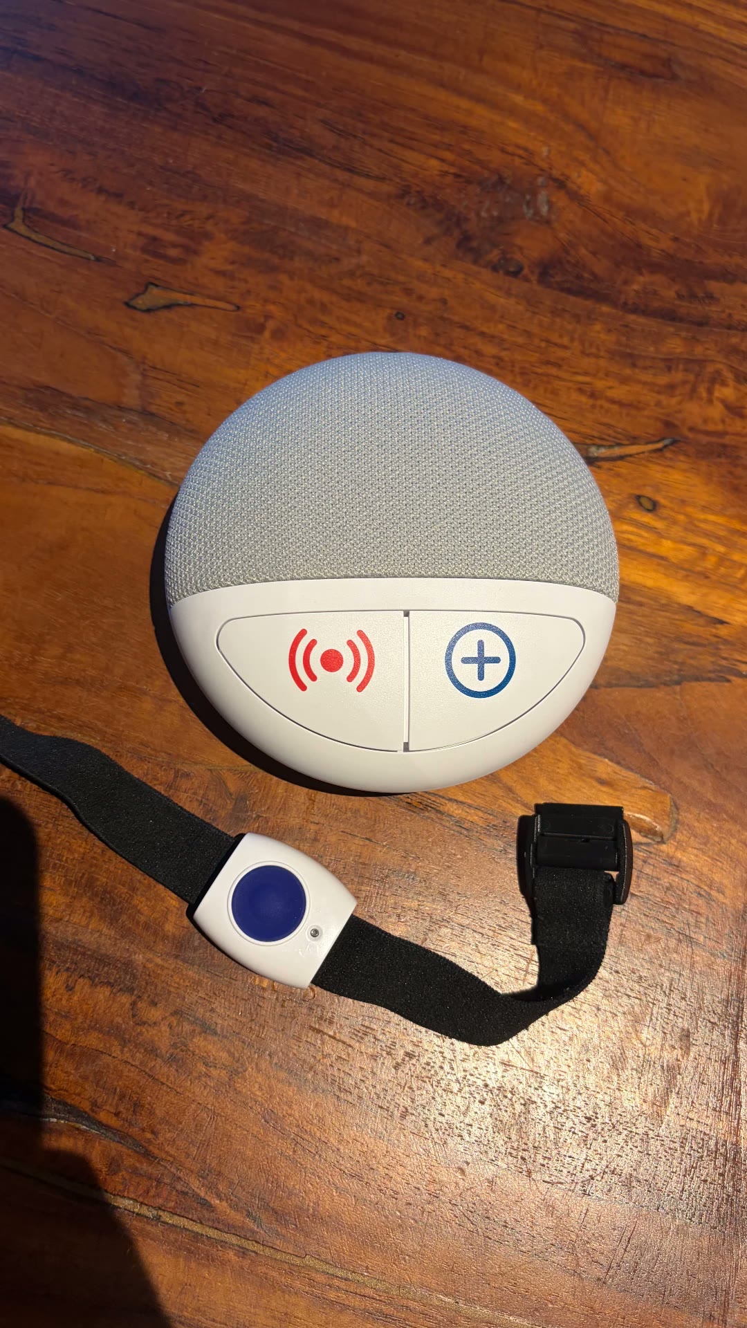 Basisstation von oben mit dem schwarzen Armband und blauem Notrufknopf daneben